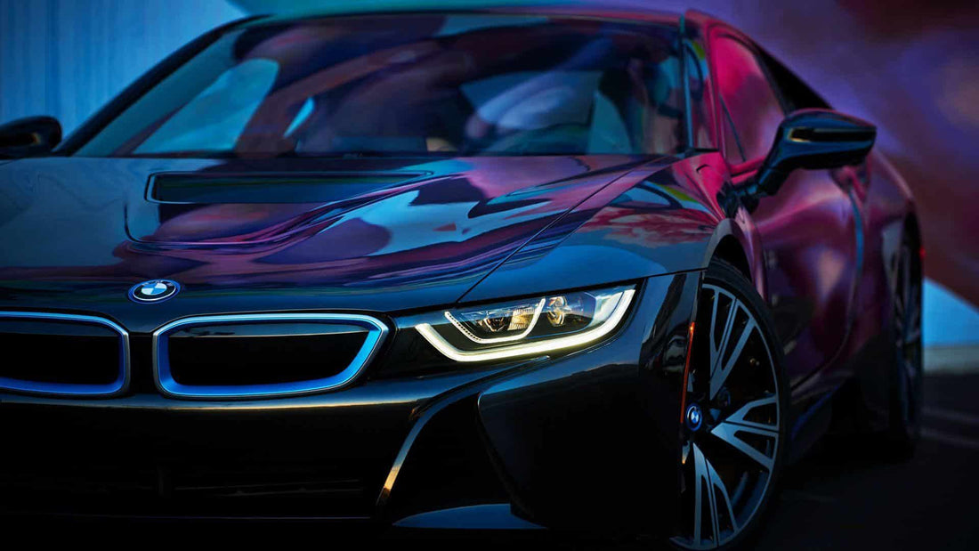 A black BMW i8 sports car with an Insurance Approved Vehicle Tracking System is parked in a dark room.